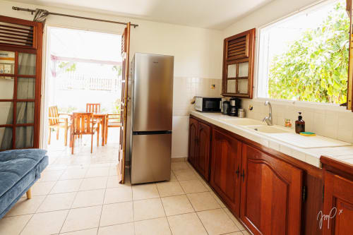 Cuisine lumineuse avec armoires en bois, réfrigérateur en acier inoxydable et vue sur la terrasse du cottage Otantik aux Caraïbes à Le Gosier