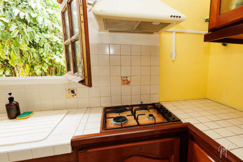 Cuisine jaune avec cuisinière à gaz, dosseret carrelé et fenêtre avec vue sur jardin au cottage caribéen Otantik, Le Gosier