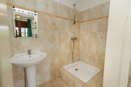 Salle de bain moderne du gîte Kaz La Brise à Otantik Caribbean, Le Gosier avec carrelage beige, lavabo sur colonne et douche ouverte