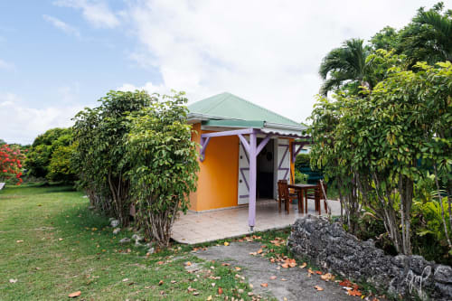 Cottage coloré d'Otantik Caribbean aux murs orange et toiture verte, niché dans un jardin tropical luxuriant à Le Gosier