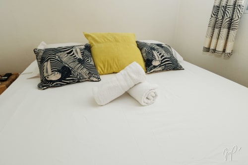 Lit blanc avec oreillers à motif zèbre noir, coussin jaune et serviettes blanches roulées à la villa Lueur du Sud