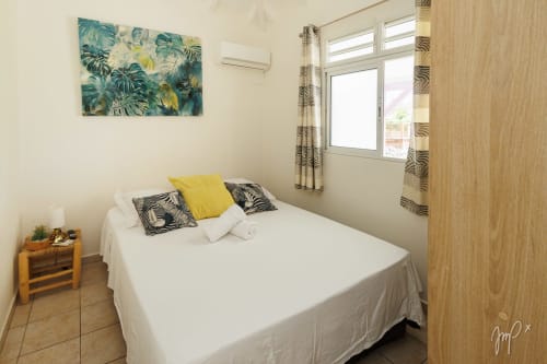 Chambre lumineuse du gîte Otantik Caribbean avec lit blanc, décor tropical et vue sur les montagnes en Guadeloupe