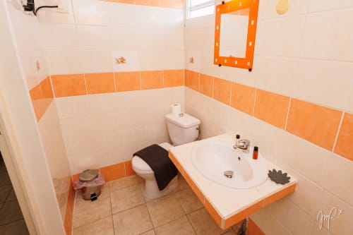 Salle de bain moderne du gîte caribéen Otantik avec carrelage orange et blanc, lavabo, toilettes et vanité en Guadeloupe