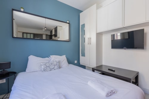 Chambre moderne de studio à Metz avec mur bleu, literie blanche, TV murale, miroir et rangements
