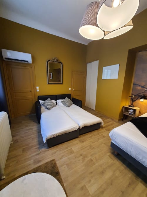 Spacieuse chambre quadruple à l'Hôtel Du Cygne à Tours avec murs jaunes, plusieurs lits et parquet
