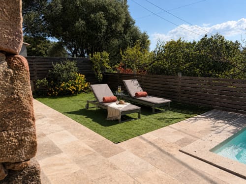Backyard with lounge chairs, manicured lawn, wooden fence, and pool edge at In Casa Conciergerie, Figari