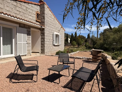 Outdoor seating area at In Casa Conciergerie cottage in Figari with black lounge chairs on gravel patio