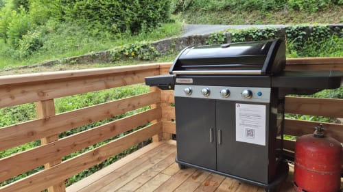 Barbecue à gaz noir sur terrasse en bois du chalet Gîte Les Boleros à Queige, vue montagne et réservoir de propane