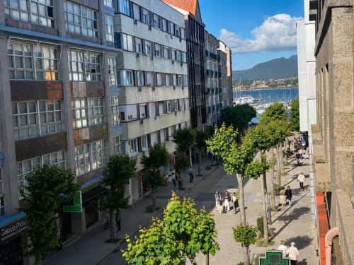 Vista de calle del pueblo costero de Baiona con edificios históricos, marina y montañas al fondo