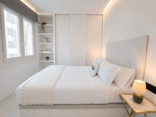 Moderno dormitorio en el apartamento Antia Mare, Baiona. Cama blanca con ropa de cama color crema, cabecero iluminado y estanterías integradas