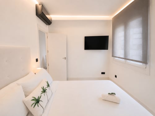 Dormitorio moderno en apartamento Antia Mare, Baiona con ropa de cama blanca, TV de pared e iluminación contemporánea