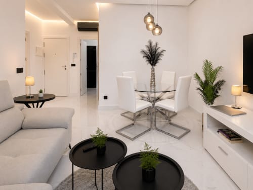 Moderno salón en Baiona con mesa de comedor de cristal, sillas blancas, lámparas colgantes elegantes y vistas a la ciudad