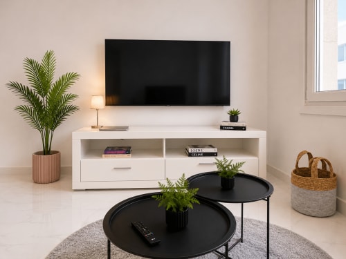 Sala de estar moderna en apartamento de Baiona con TV montada en pared, consola blanca, mesas redondas negras y plantas en maceta