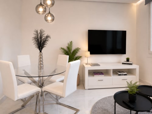 Moderno salón con TV, mesa de comedor, lámparas colgantes y plantas en Holibai Baiona