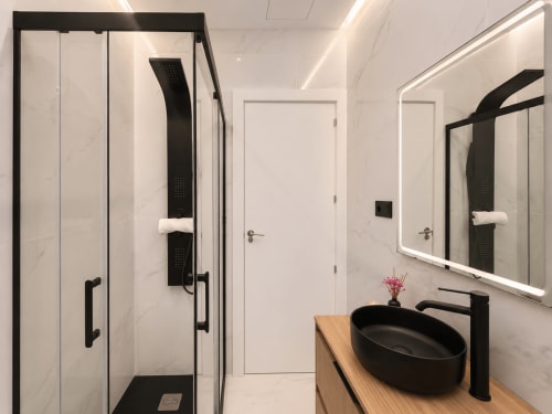 Baño moderno en apartamento Antia Mare, Baiona con accesorios negros, azulejos de mármol y espejo iluminado