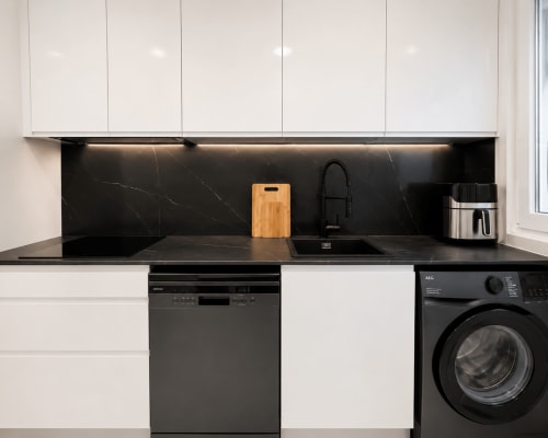 Cocina moderna en apartamento Antia Mare, Baiona con backsplash de mármol negro, armarios blancos, lavavajillas y lavadora