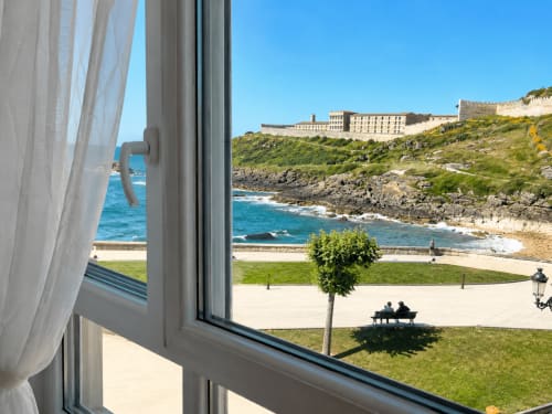 Vista desde la ventana del apartamento Holibai: costa de Baiona con playa, fortaleza y plaza arbolada