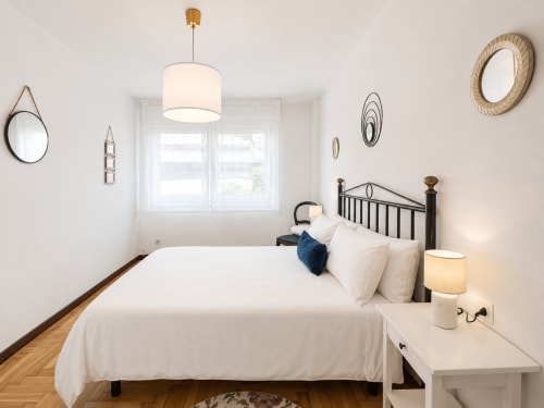Dormitorio moderno y luminoso en apartamento Holibai con ropa de cama blanca, estructura de cama de metal negro, piso de madera y decoración náutica