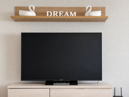 Estante de madera con texto 'DREAM' y decoraciones de cisnes blancos sobre TV de pantalla plana en apartamento Holibai, Baiona