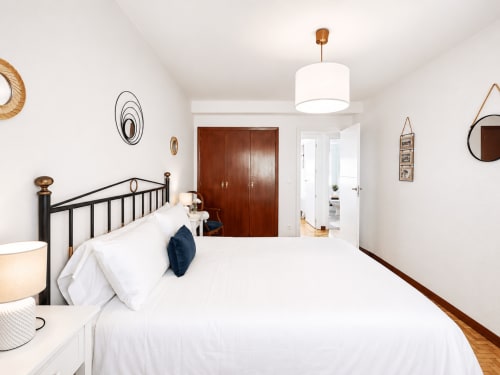 Dormitorio moderno en apartamento familiar Morriña, Baiona con ropa de cama blanca, estructura metálica, armario de madera y luz natural