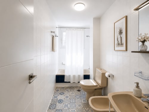 Baño moderno en el apartamento Morriña de Holibai, Baiona, con azulejos blancos, doble lavamanos, inodoro y ducha