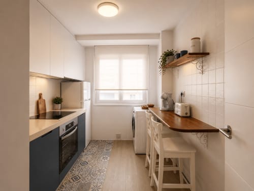 Cocina moderna en apartamento Morriña, Baiona con muebles blancos, encimeras oscuras y zona de bar de madera