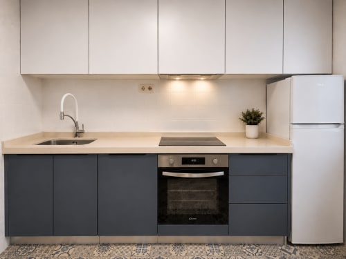 Cocina moderna del apartamento Holibai en Baiona con muebles oscuros, encimera clara, estufa, fregadero y refrigerador
