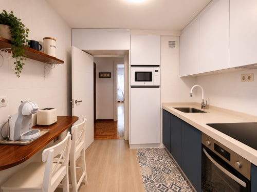 Cocina americana moderna en apartamento Morriña de Holibai, Baiona con armarios blancos, encimera de madera y acero inoxidable