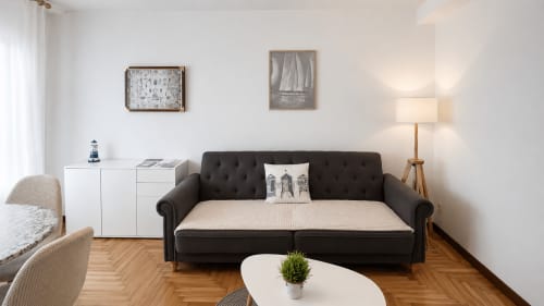 Sala moderna del apartamento Holibai en Baiona con sofá negro, mesa de café blanca, pisos de madera y decoración náutica