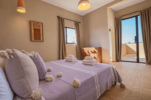 Chambre spacieuse du Riad Arkaya à Essaouira avec literie violette, serviettes blanches et accès à la terrasse surplombant le jardin