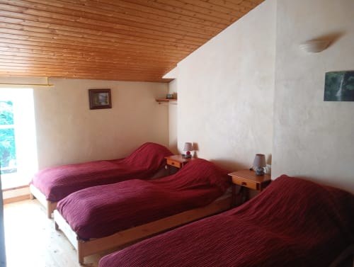 Trois lits simples avec literie bordeaux dans la chambre accessible du gîte La Faerie, Grand'landes