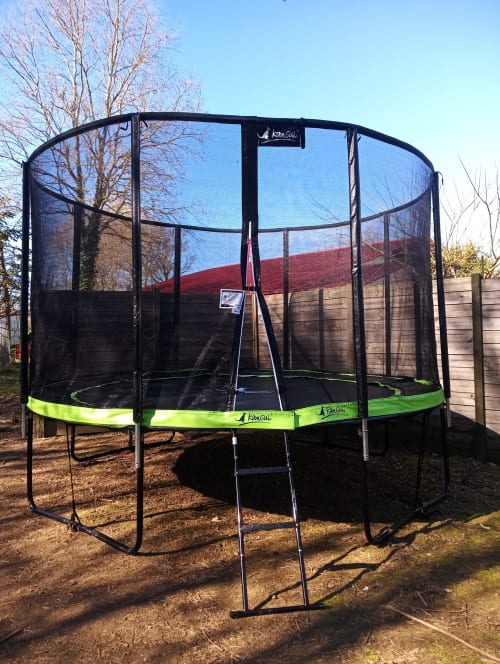 Trampoline noir avec rembourrage vert et filet de sécurité dans le jardin de La Faerie cottage, Grand'landes