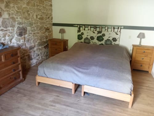 Chambre spacieuse de la cottage La Faerie avec lit en bois, murs en pierre et tête de lit avec vue sur le jardin décorée de motifs de feuilles vertes