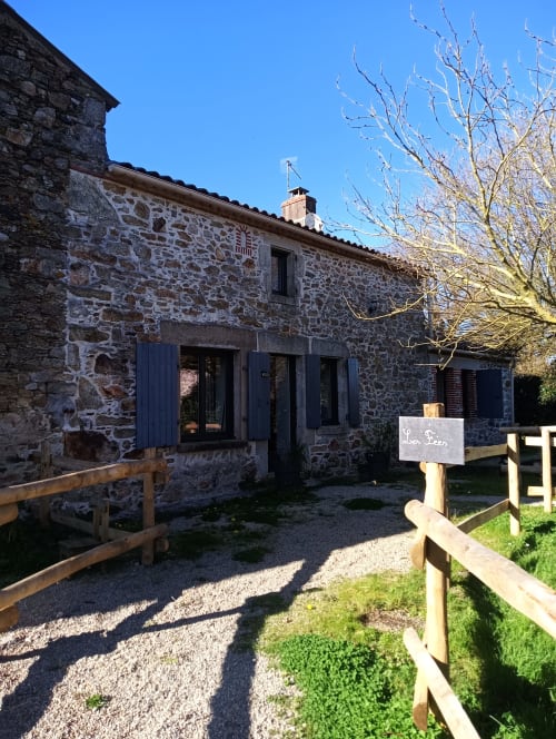 Maison d'hôtes La Faerie à Grand'landes avec volets bleus, clôture en bois et arbres nus sous un ciel bleu dégagé
