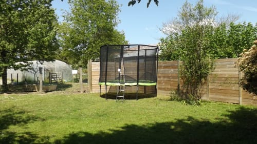 Jardin spacieux de la chaumière La Faerie avec trampoline, clôture en bois et pelouse verdoyante à Grand'landes