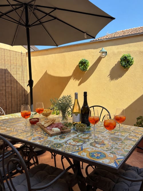 Accogliente zona pranzo all'aperto presso l'appartamento Sicily In Home a Catania, con tavolo decorato a piastrelle, bicchieri di vino e stuzzichini