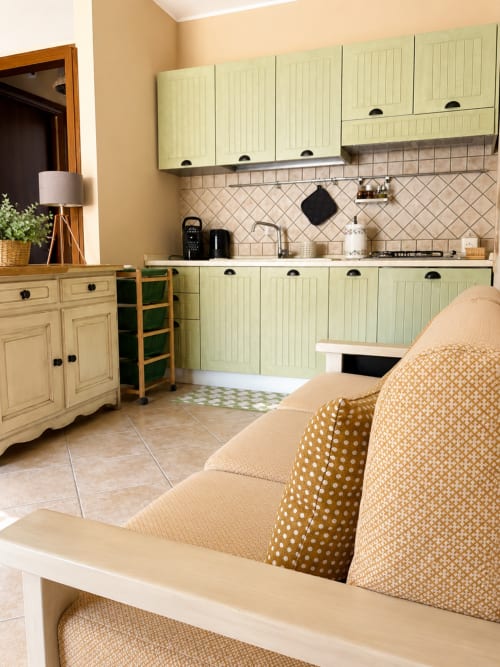 Luminosa zona cucina-soggiorno nell'appartamento In Home di Sicilia, Catania, con mobili verde salvia, muri color crema e motivi decorativi