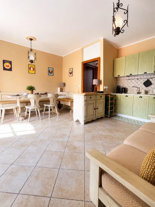 Luminosa zona cucina-pranzo nell'appartamento Almarina di Catania, con pareti gialle, arredamento bianco, ante verdi e piastrelle