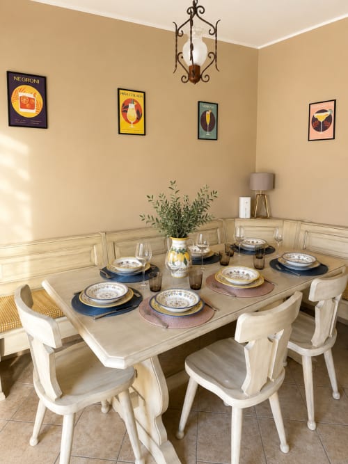 Elegante sala da pranzo nell'appartamento di Catania con sedie bianche, tavolo in legno, mise en place e poster di cocktail su beige