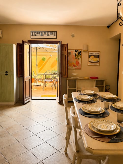 Elegante sala da pranzo con tavolo apparecchiato che si apre sul soleggiato patio giallo, appartamento Sicily In Home a Catania