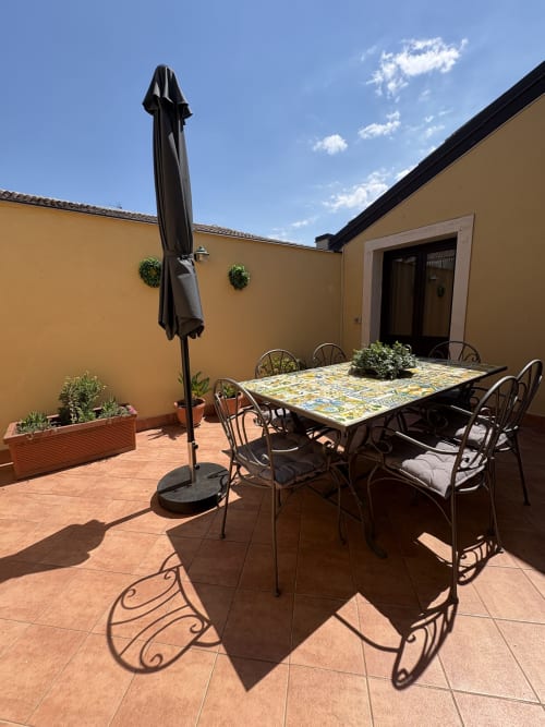 Terrazza soleggiata dell'appartamento Sicily In Home a Catania con tavolo da pranzo, ombrellone nero e muri gialli