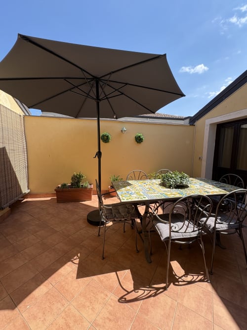 Terrazza soleggiata con tavolo da pranzo, ombrellone nero e piante in vaso all'appartamento Sicily In Home di Catania