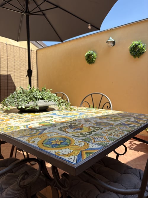Terrazza esterna di Sicily In Home a Catania con tavolo decorativo in ceramica, ombrellone nero, vasi di piante e finiture color ocra
