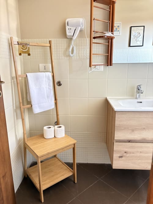Bagno dell'appartamento Sicily In Home a Catania con scaletta in legno, asciugamani bianchi, carta igienica, piastrelle, lavandino e
