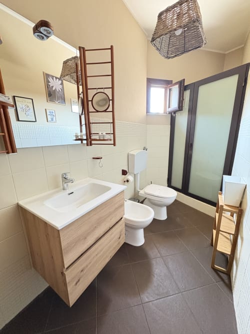 Ampio bagno in appartamento In Home a Sicilia, Catania, con vanità in legno, lavabo bianco, bidet, water e doccia moderna