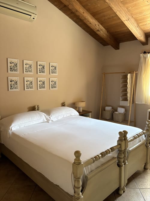 Luminosa camera da letto a Sicily In Home Almarina con travi in legno, biancheria bianca e parete galleria d'arte a Catania.