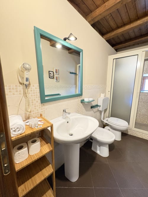 Bagno moderno con specchio cornice teal, lavabo a colonna, wc, bidet e mobili in legno in Sicilia