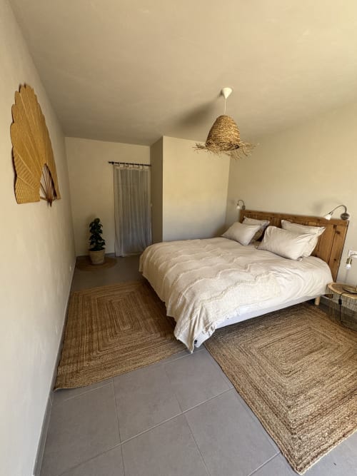 Chambre minimaliste au Domaine d'Olga à Aniane avec lit bois, tapis naturels et suspension tissée
