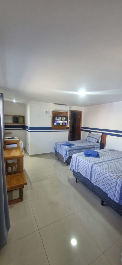 Triple suite bedroom at Praieira Pousada hostel in Itacaré with two beds, TV, and modern amenities