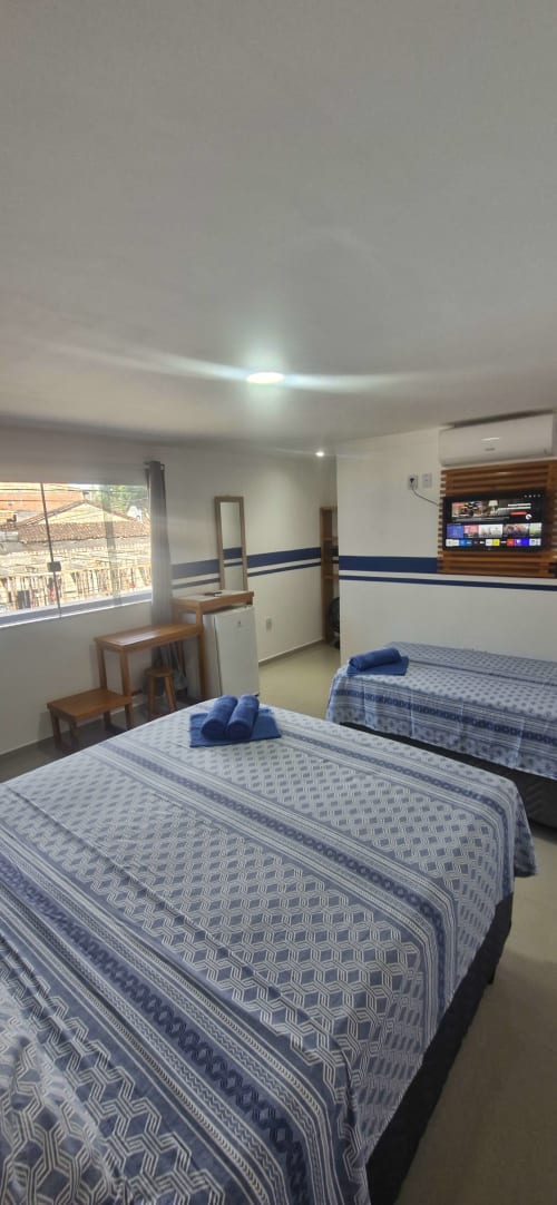 Triple queen suite at Praieira Pousada hostel in Itacaré with two beds, desk, TV, and ocean view window